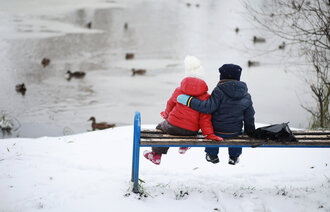 Bildet viser to barn som sitter på en benk og ser på et vann med ender på