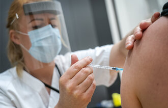Vaksinesprøyte settes i arm av helsepersonell.