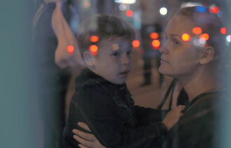 Bildet viser en kvinne som stirrer ut av et vindu med et barn på fanget