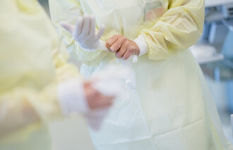 Bildet viser helsearbeidere i gule frakker som tar på hansker.