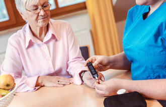 Bildet viser en sykepleier som måler blodsukkeret på en eldre kvinne