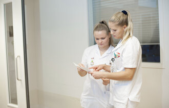 Bildet viser to sykepleiere som står og ser på et ark.