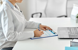 Bildet viser et helsepersonell som sitter foran en pc og fyller ut et skjema