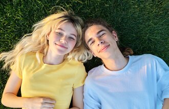 Bildet viser to smilende ungdommer som ligger på gresset