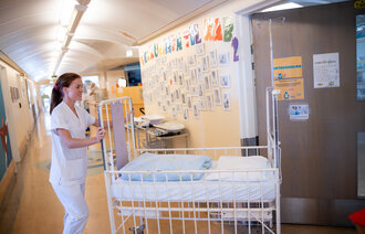 Bildet viser en sykepleier som triller en barneseng i en sykehuskorridor.
