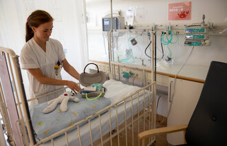 Bildet viser en sykepleier som legger frem en dukke og et førstehjelpsskrin laget av pussbekken.