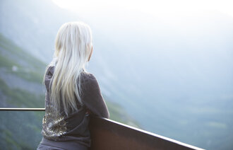 Bildet viser en ung lyshåret jente, bakfra, som ser utover fra en høyde