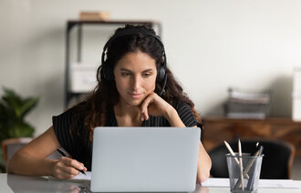 En ung kvinne med hodetelefoner ser på PC-en