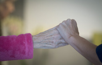Bildet viser en sykepleier som holder et eldre menneske i hånden