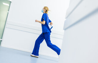 Bildet viser en sykepleier med munnbind som løper i korridoren