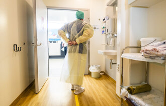 Bildet viser et helsepersonell utenfor en sluse som ikler seg smittevernutstyr.