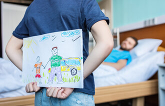Barn gjemmer tegning bak ryggen ved fars sykeseng.
