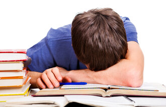Bildet viser en fortvilet student som hviler hodet på pulten mens han er omgitt av bøker