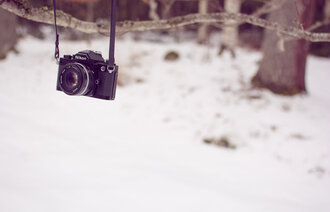 Bildet viser et fotoapparat som henger på en gren i skogen. Det er vinter.