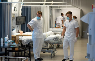 Bildet viser to sykepleierstudenter på et sykehus. De øver på en simuleringsdukke