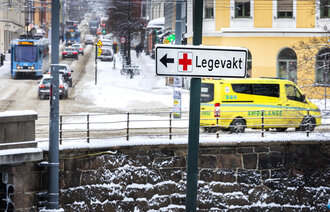 Bildet viser trafikkbildet i Oslo. Et skilt peker til Legevakta, mens en ambulanse kjører forbi