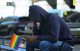 Bildet viser et ungt menneske med hodet bøyd. Vedkommende har pride-flagget i hånden.