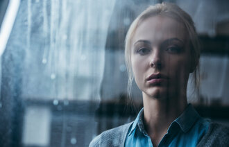 Bildet viser en trist kvinne som ser ut av et vindu. 