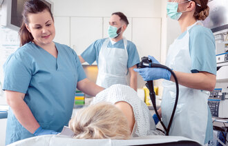 Bildet viser en pasient som tar koloskopi. Rundt pasienten står en sykepleier som trøster, og to endoskopører som ser på en skjerm