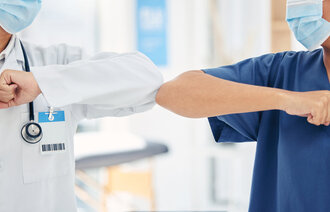 Bildet viser utsnittet av en lege og en sykepleier som korona-hilser med albuene