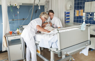 Bildet viser en sykepleier og en sykepleierstudent ved sengen til en pasient.