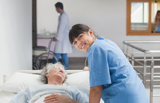 Bildet viser en sykepleier som lener seg over en pasient mens hun smiler til fotografen