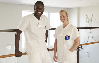 Bildet viser en mannlig og en kvinnelig sykepleier som smiler.