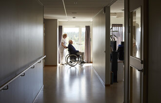 En kvinnelig sykepleier skyver en eldre pasient i rullestol