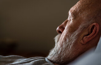 Bildet viser en eldre mann i profil med lukkede øyne. Han ligger i sengen.