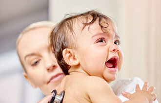 Bildet viser et lite barn som gråter mens en sykepleier lytter på ryggen til barnet
