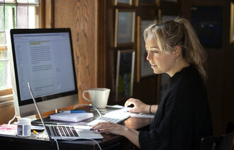 Bildet viser en kvinne som sitter hjemme ved en datamaskin.