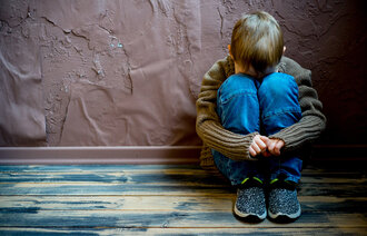 Bildet viser et lite barn som sitter mot en vegg med opptrukne knær og skjuler ansiktet sitt.