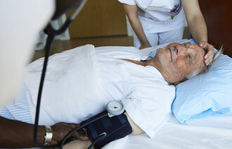 Bildet viser en sengeliggende mannlig pasient som får pleie av to sykepleiere