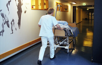 Bildet viser en mannlig sykepleier som triller en pasientseng i sykehus
