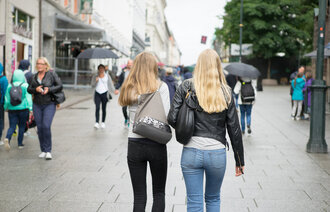 Bildet viser to unge kvinner, fotografert bakfra, som går på gaten