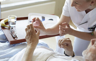 Bildet viser en kvinnelig sykepleier som gir en sengeliggende pasient medisin.