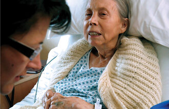 Bilde viser pleier hos en eldre dame som ligger i sengen.