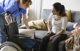 Bildet viser en sykepleier i hjemmetjenesten som hjelper en rullestolbruker