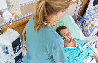 Bildet viser en intensivsykepleier som overvåker en pasient i en sykehusseng