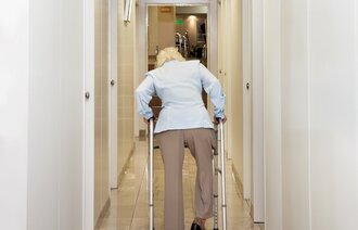 Bildet viser en eldre dame som går bortover en sykehjemskorridor