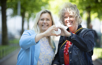 Bildet viser Ina Giske og Hege Kornberg Christensen. De smiler og sammen former de et hjerte med hendene sine.