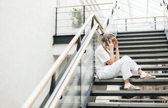 Bildet viser en sykepleier som sitter i en trapp, snakker i telefonen og ser sliten ut