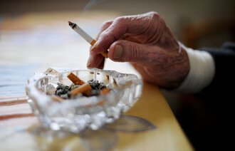 Bildet viser en hånd som holder en sigarett over et askebeger