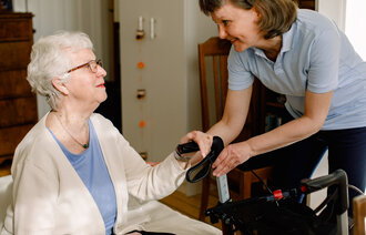 Bildet viser en kvinnelig helsearbeider som har øyekontakt med en eldre kvinnelig pasient som sitter ned.