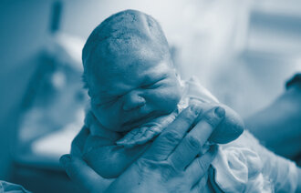 The photo shows a newborn baby being held by a couple of hands