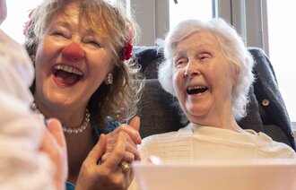 Bildet viser en klokkeklovn på et sykehjem sammen med en eldre kvinne. Kvinnen ler.