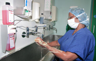 The photo shows a surgical nurse washing her hands before surgery
