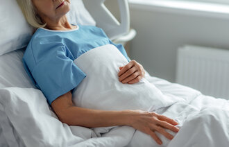 Bildet viser en eldre kvinne i en sykehusseng