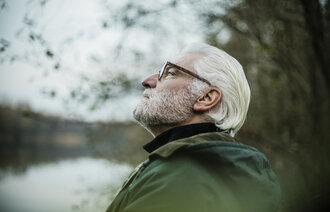 Bildet viser en eldre mann som ser tankefullt ut i luften ved et vann
