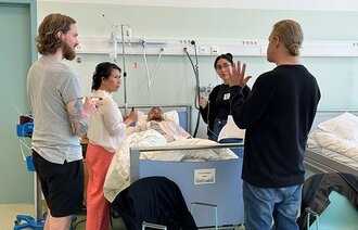 Bildet viser helsepersonell som snakker sammen ved en pasient.
